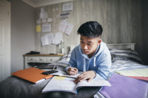 teenage boy doing homework on bed and a look at how school affects mental health among teens